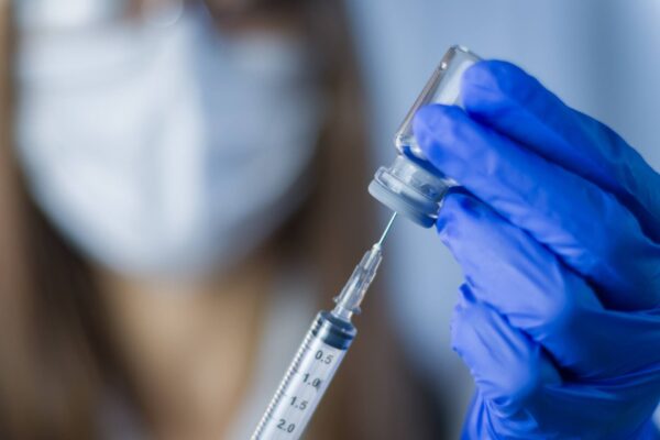 Preventing sterile injectable manufacturing risks - Doctor holding a vial of injectable medication while transferring it into a syringe.